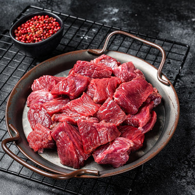 Raw venison pieces on a metal tray with red peppercorns in the background