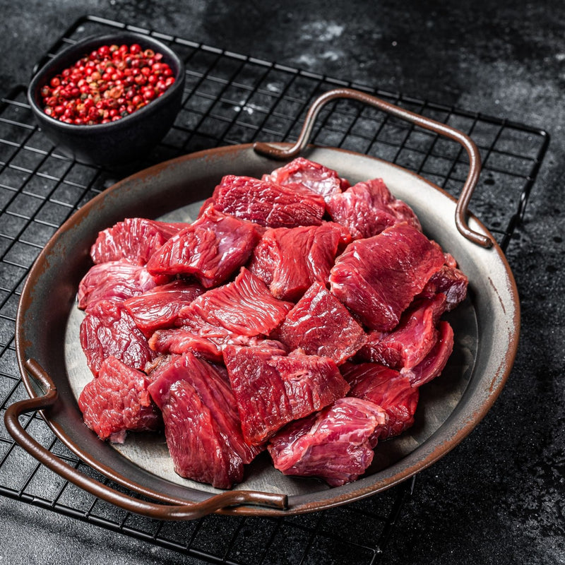 Raw venison pieces on a metal tray with red peppercorns in the background