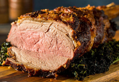 Sliced roasted beef with a crispy exterior on a wooden cutting board.