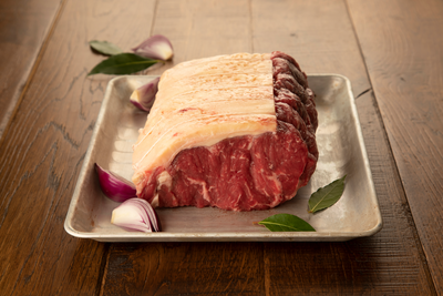 A rolled sirloin steak placed on a metal tray, surrounded by sliced onions and thyme leaves, set against a wooden background.