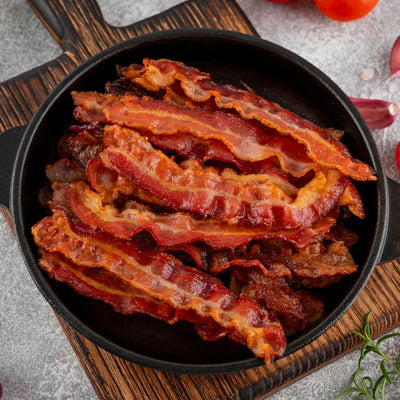Slices of cooked streaky bacon in a black skillet on a wooden board