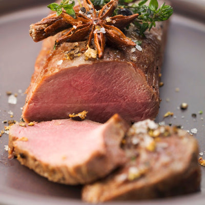 Roasted venison loin garnished with herbs and spices on a rustic plate